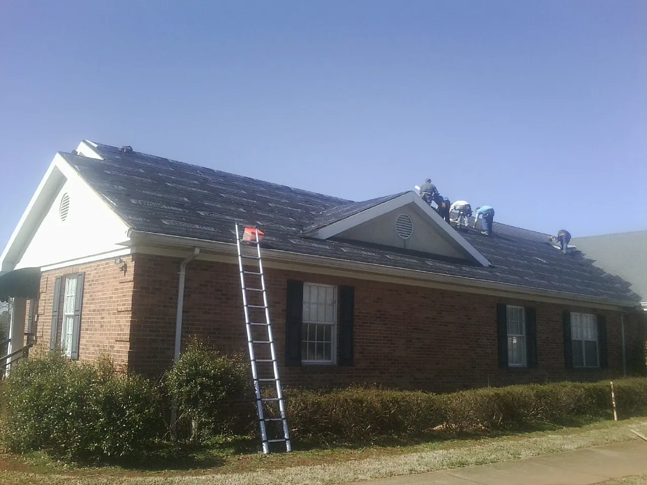 Crew tearing shingles off a brick ranch roof with a ladder set — Metal Roof Repair work by our crew in Yadkinville