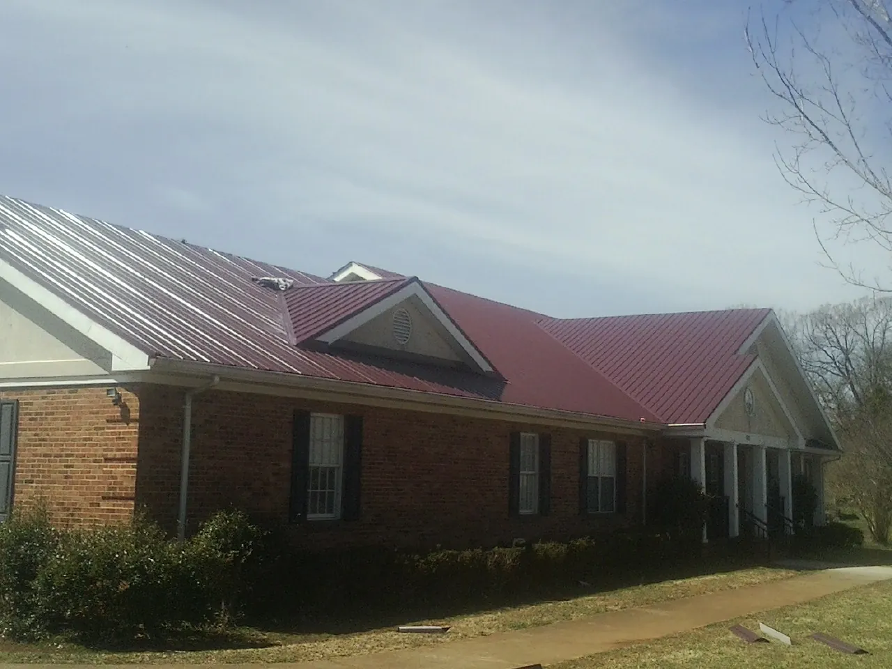 Red metal roof with gabled entries on a long brick building, from a Hail Damage Roof Repair job in Yadkinville