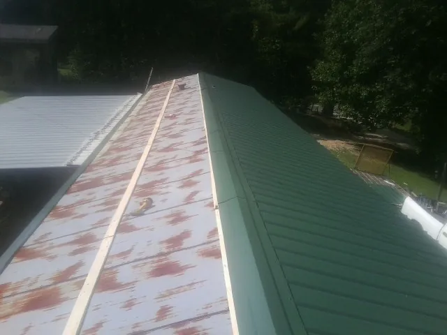 Old rusted panels beside newly installed green metal roofing — Wind Damage Roof Repair by Roofing Brothers in Yadkinville