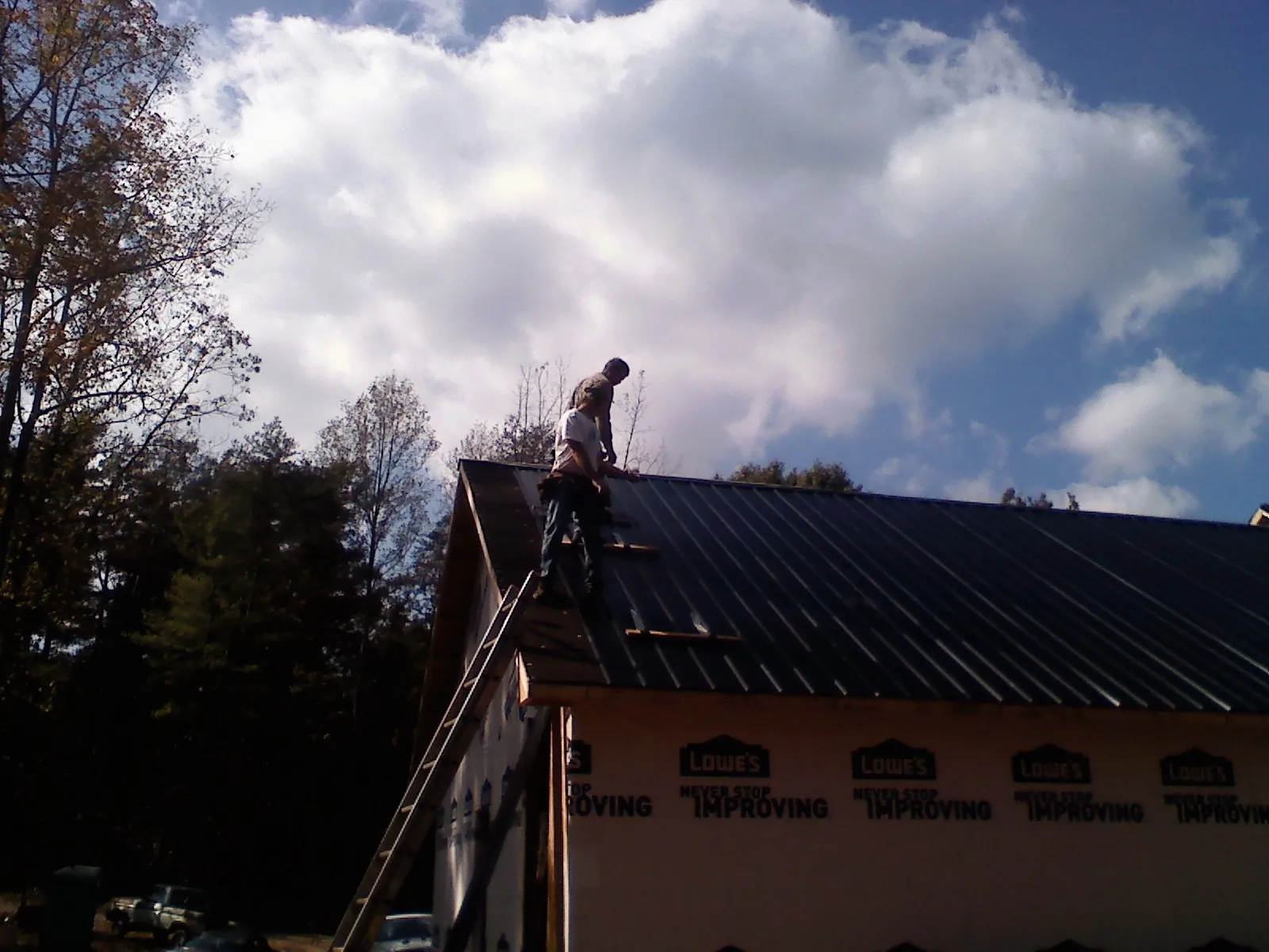 Roofer fastening dark metal panels high against a cloudy sky, from a Roof Inspection job in Yadkinville