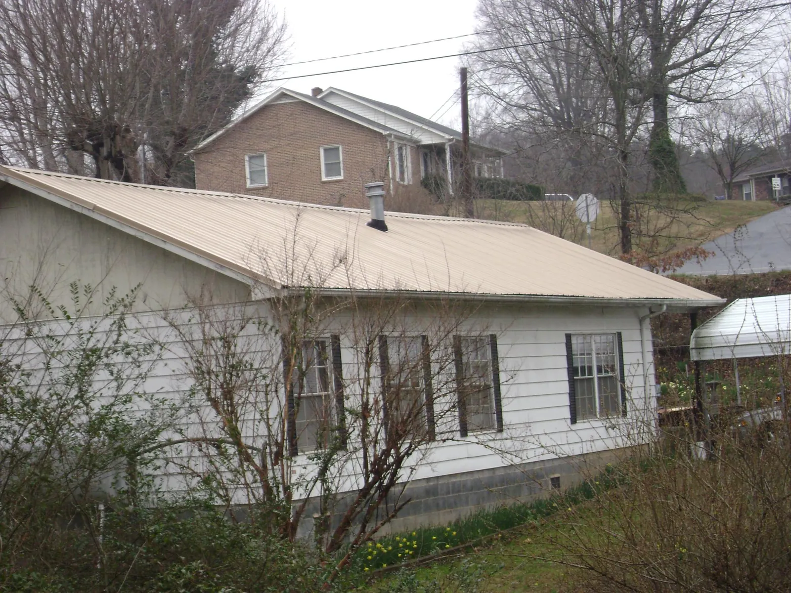 Tan metal roof on a white sided house set into a hillside — Commercial Roofing by Roofing Brothers in Yadkinville